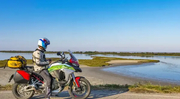 Motociclista con moto da enduro ferma sul ciglio di una strada sterrata, con sullo sfondo il paesaggio del Delta del Po.