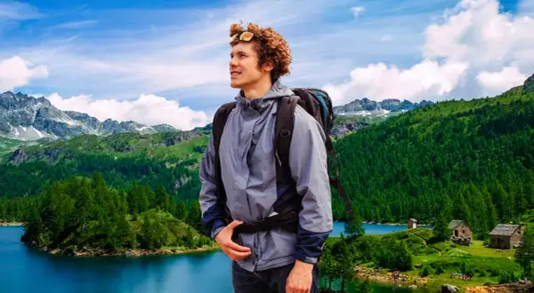 Giovane escursionista con zaino ammira un paesaggio alpino con laghi e boschi nel Piemonte.