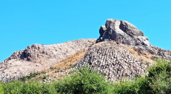 Rocciosa cresta nella Planargia, Sardegna, sotto un cielo azzurro. Vegetazione verde rigogliosa in primo piano.