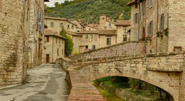 Antico ponte in pietra attraversa un ruscello, fiancheggiato da case in pietra e vicoli stretti, tipici dei paesi in Umbria.