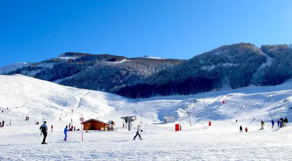 Piste innevate e sciatori in azione, un perfetto esempio di dove si scia in Abruzzo. Montagne innevate e cielo azzurro.