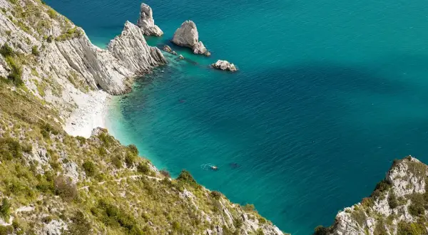 Scogliere bianche e mare turchese in una splendida località sulla riviera del Conero. Una piccola spiaggia nascosta e faraglioni emergono dall'acqua cristallina.