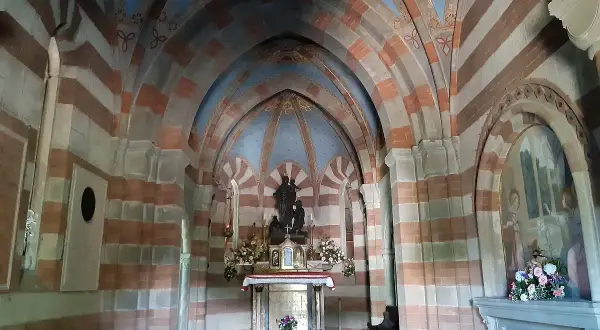 Interno di una cappella con volte a crociera a strisce rosse e bianche. Al centro, un altare con statue e fiori. Un esempio di cosa vedere a Berceto.