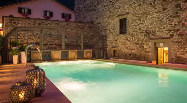 Piscina termale illuminata da lanterne, con cascate d'acqua e un edificio in pietra. Un'oasi di relax che ricorda le terme della Riviera Romagnola.