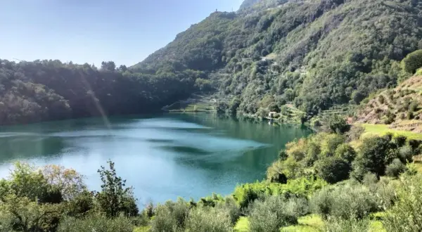 Lago alpino dalle acque verdi, circondato da boschi rigogliosi e terrazzamenti coltivati. Un angolo terme naturale e sereno.