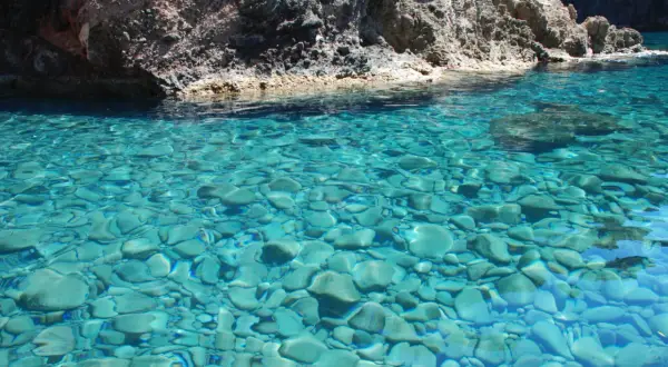 Acque cristalline del mare di Capraia, con fondale roccioso e ciottoli visibili sotto la superficie turchese.