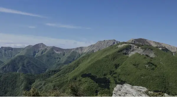 Panoramica dei colli bolognesi in moto, con montagne verdi sotto un cielo azzurro.