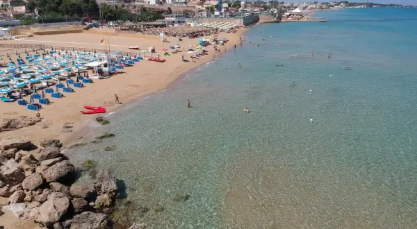 Una spiaggia affollata con lettini e ombrelloni, bagnanti in acqua e due kayak rossi sulla sabbia. Il noto mare cristallino invita a un tuffo.