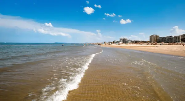Onda leggera sulla sabbia dorata, con bagnanti e hotel sullo sfondo. Un classico giorno di **mare Emilia Romagna**.