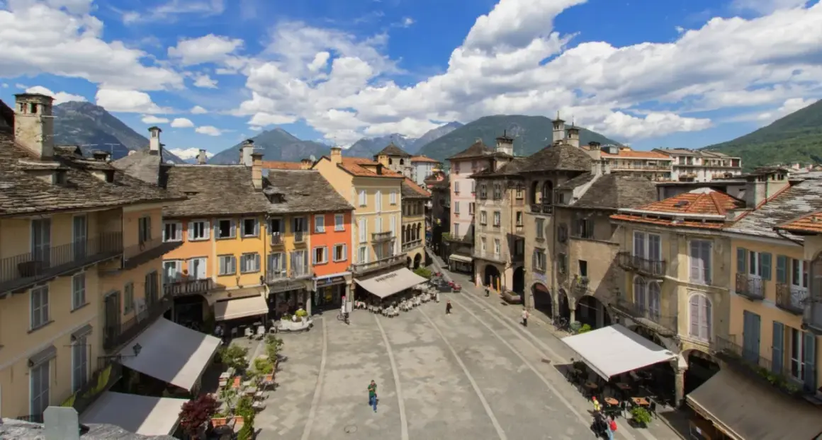 Piazza colorata con montagne sullo sfondo, un assaggio di dove si trova Domodossola.