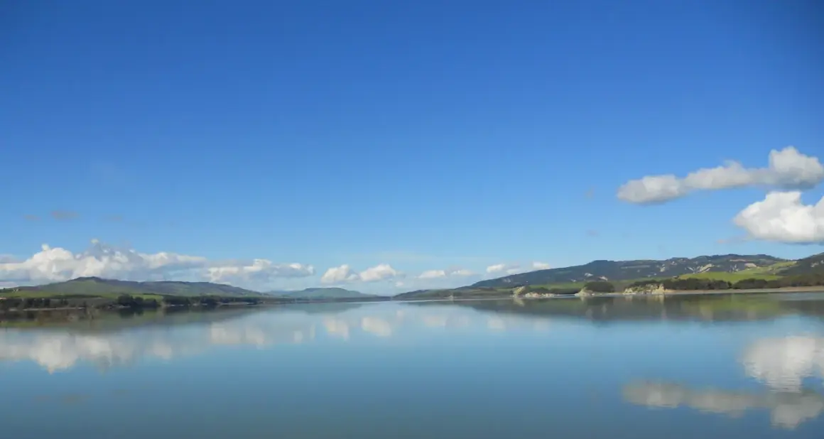 Lago calmo con riflessi di colline verdi e cielo azzurro. Un'ottima meta per scoprire cosa vedere vicino Matera.