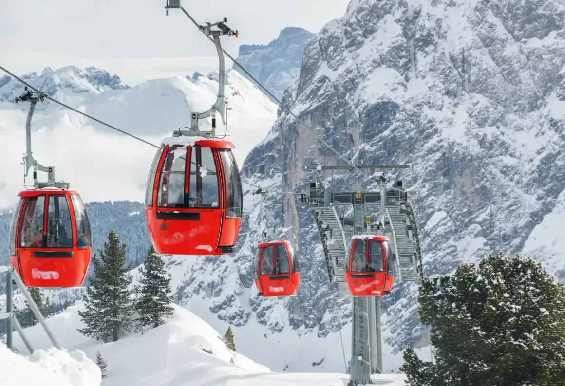 Cabine rosse su un impianto di risalita in Trentino, perfette per esplorare le località sciistiche economiche. Montagne innevate e pini sullo sfondo.