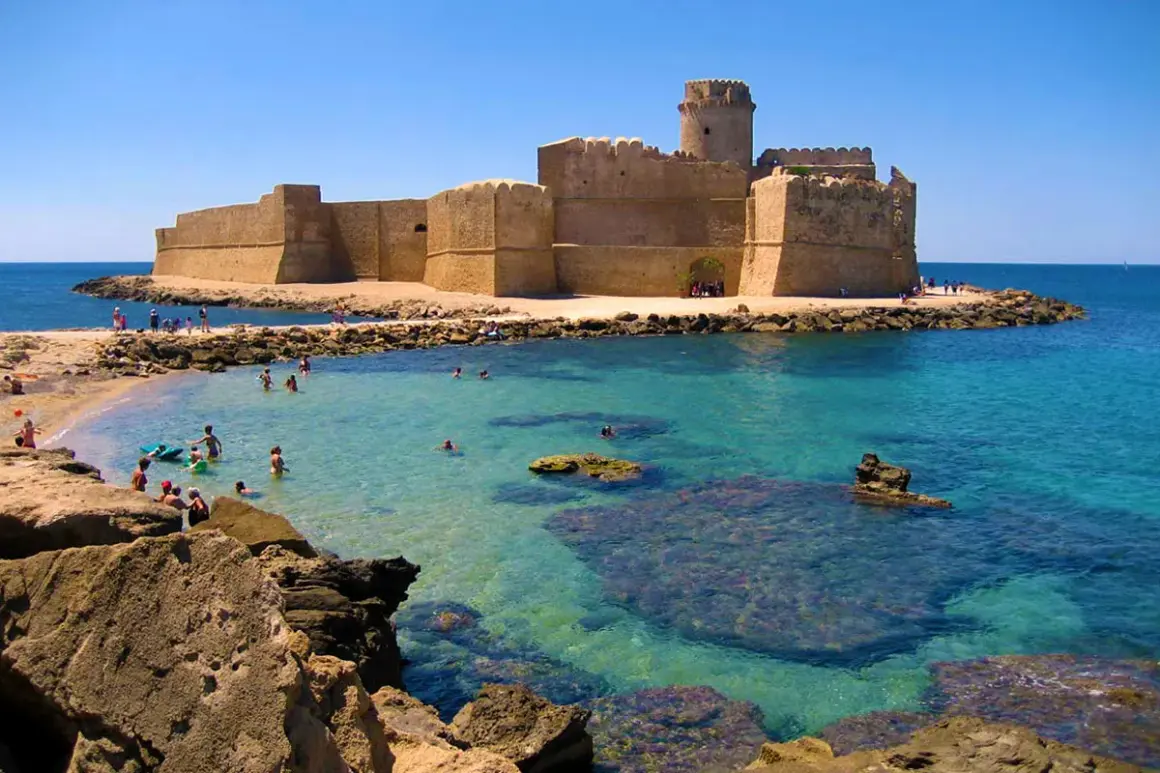 Castello Aragonese su una delle migliori spiagge calabria, con acque cristalline e bagnanti che si godono il sole.