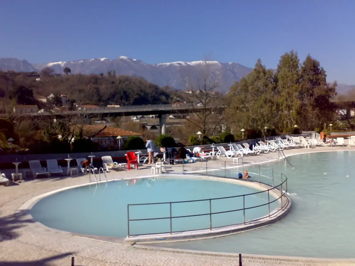 Piscine termali con lettini e ombrelloni, montagne innevate sullo sfondo. Un'oasi di relax per godersi le contursi terme gratis.