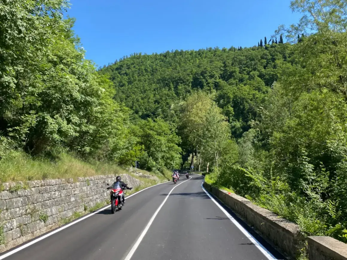 Motociclisti sfrecciano su strade panoramiche dell'Emilia Romagna, tra colline verdi e cielo azzurro.