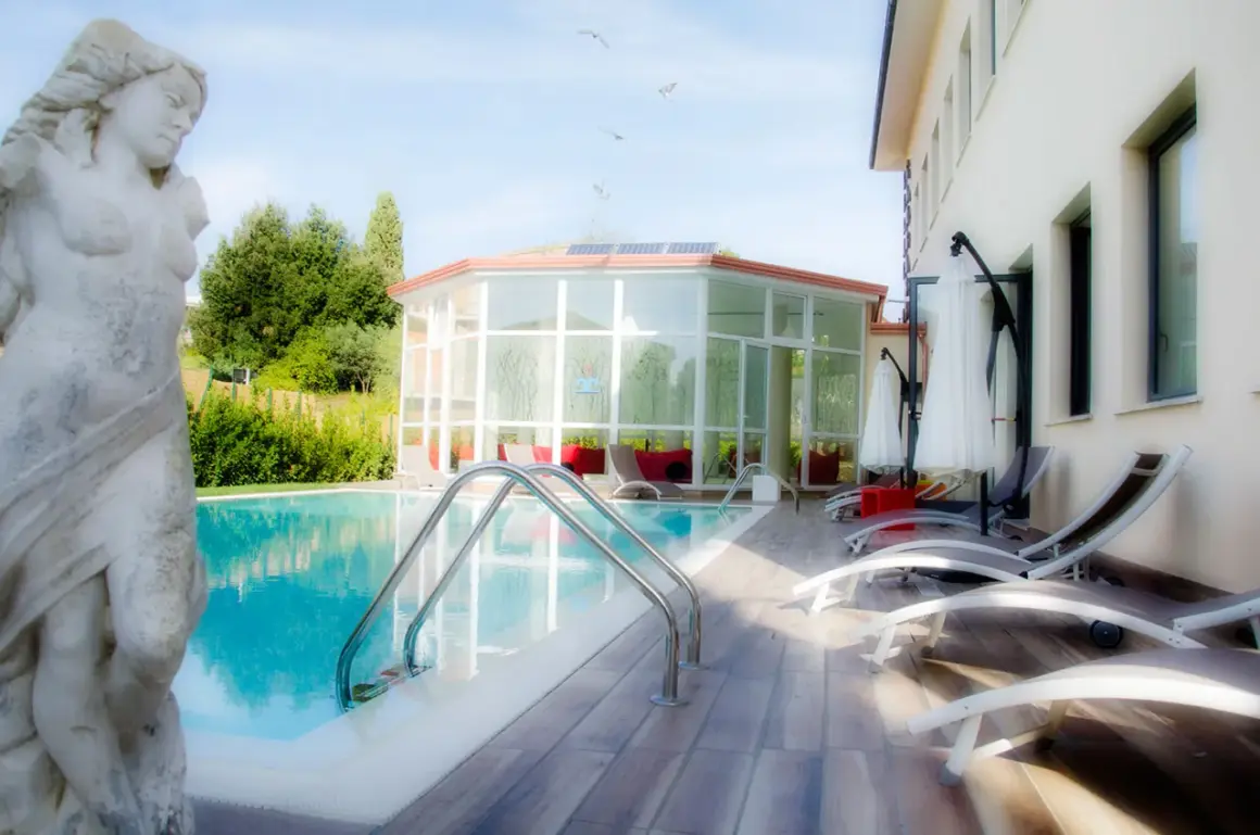 Statua classica vicino alla piscina, con un edificio moderno e un giardino lussureggiante. Un'oasi di relax a Gambassi Terme.