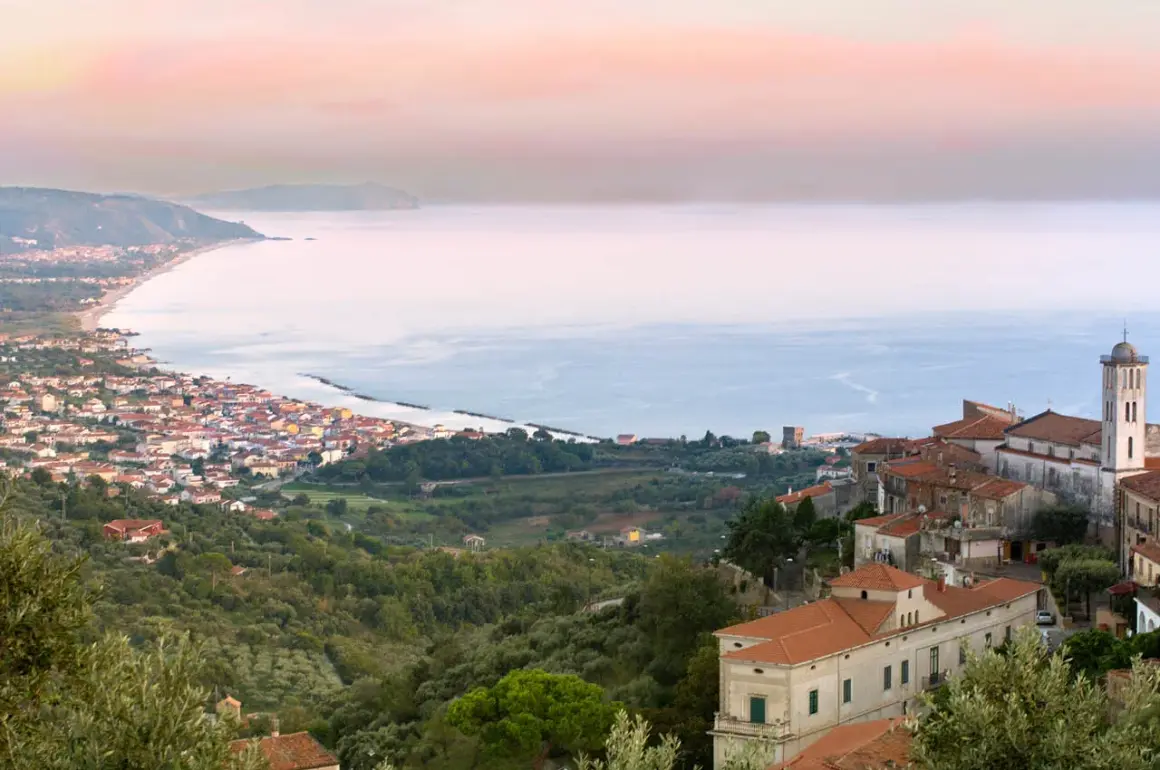 Vista panoramica di un borgo costiero nel Cilento, con case arroccate su una collina che scende verso il mare azzurro.