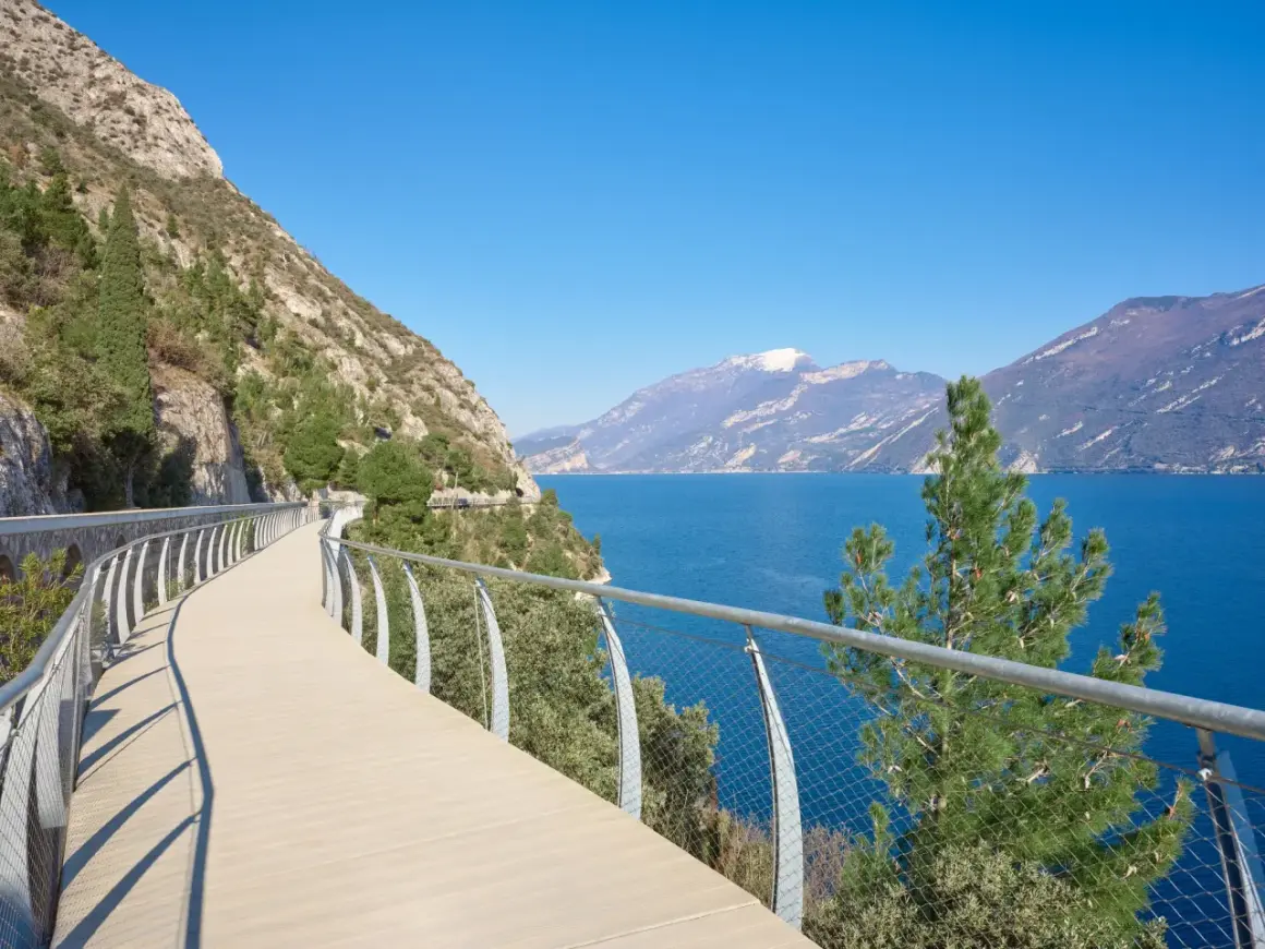 Una moderna ciclabile a picco sul lago, con montagne sullo sfondo. Potrebbe essere la ciclabile più bella d'Italia.
