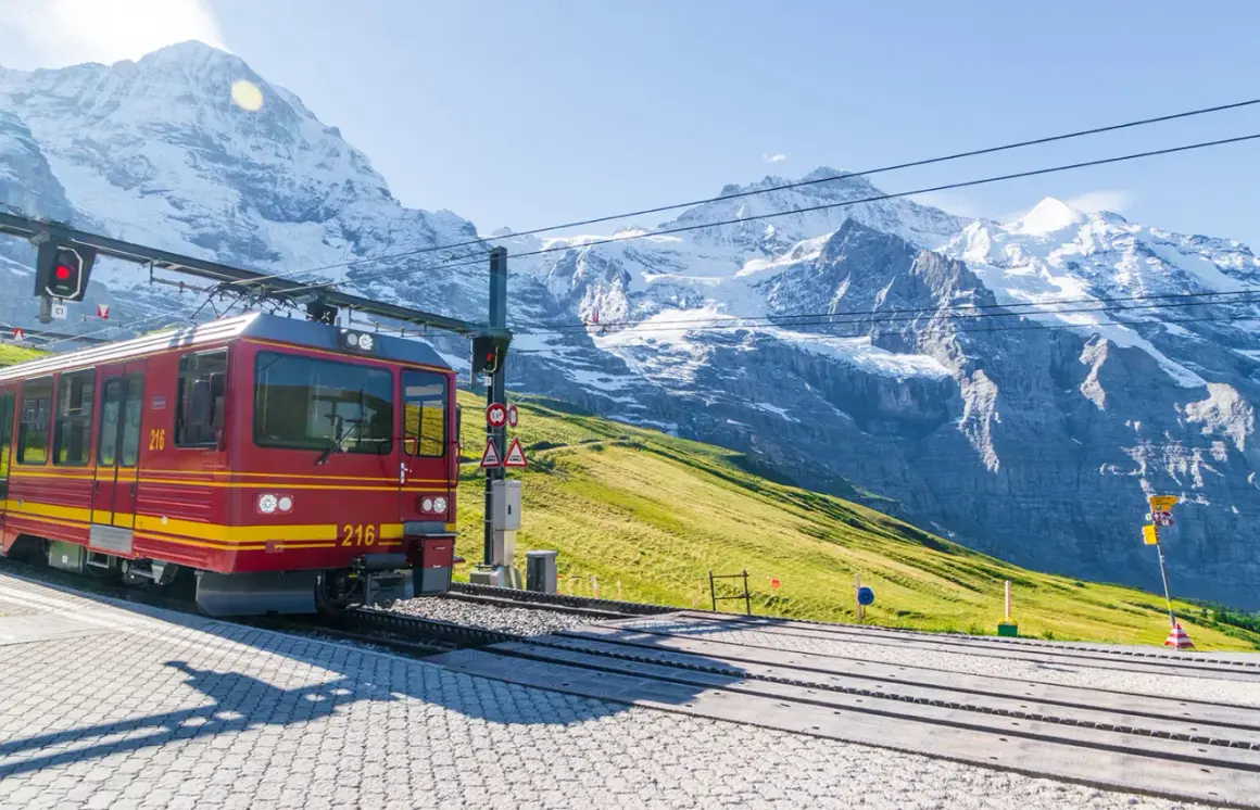 Treno rosso su binari alpini, ideale per raggiungere località di montagna raggiungibili in treno da Bologna, con maestose cime innevate sullo sfondo.