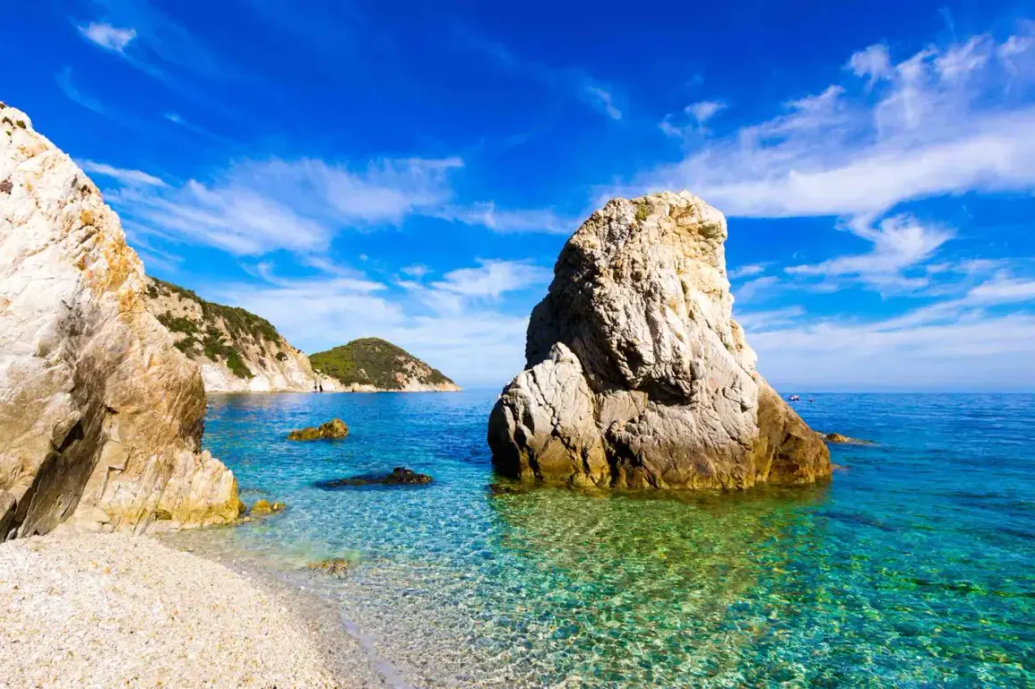 Scogliera imponente su una spiaggia di ciottoli, mare cristallino e isole verdi all'orizzonte. Una splendida località di mare tra Lazio e Toscana.