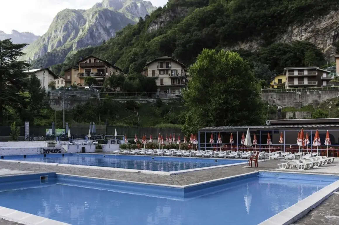 Piscine azzurre a Sant'Omobono Terme, con montagne verdi sullo sfondo e case arroccate.