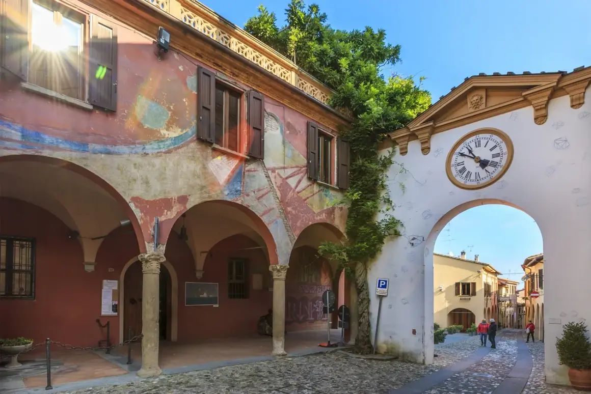 Un arco con orologio conduce a una strada acciottolata, un invito a scoprire i borghi da visitare vicino a Forlì.