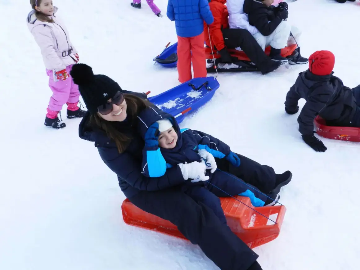 Mamma e bambino felici sciano in Abruzzo con slittino. Altri bambini giocano sulla neve.
