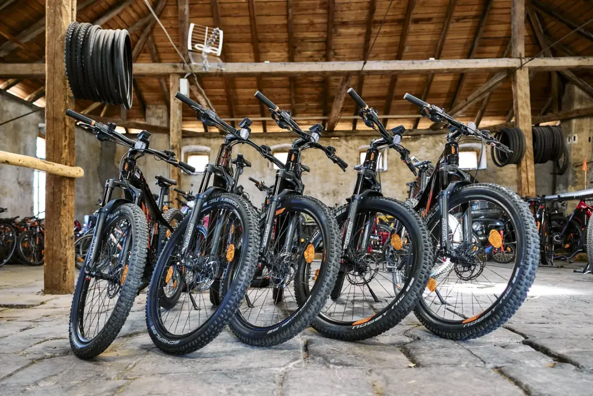 Bici in montagna pronte per l'avventura. Diverse mountain bike nere con dettagli arancioni, parcheggiate in un fienile con travi in legno.