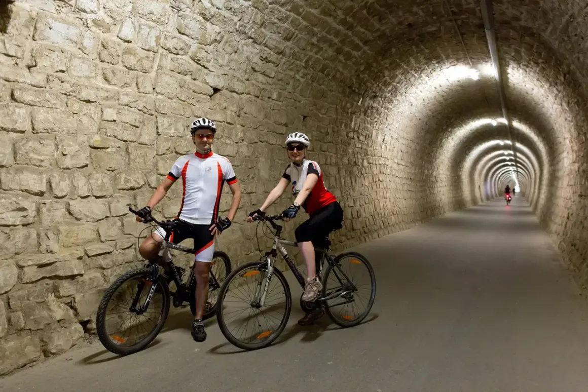 Coppia in bicicletta nel tunnel del **parenzana tracciato**, un percorso suggestivo tra storia e natura.