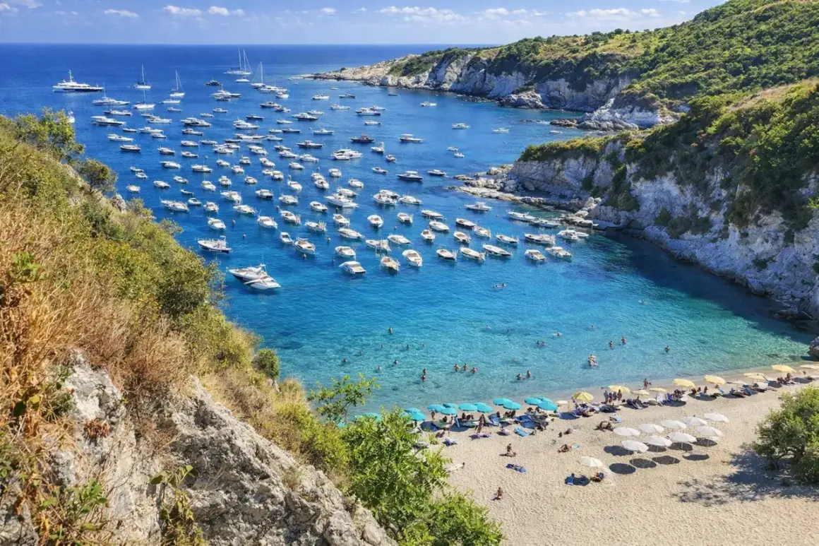 Baia con acque cristalline e numerose barche ormeggiate. La spiaggia di sabbia dorata è animata da ombrelloni e bagnanti. Un vero paradiso tra le spiagge di Ponza.
