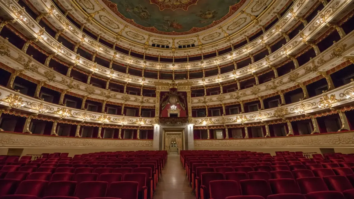 Interno di un teatro storico con file di poltrone rosse e palchi dorati. Un luogo da scoprire tra le cose da vedere a Parma gratis.