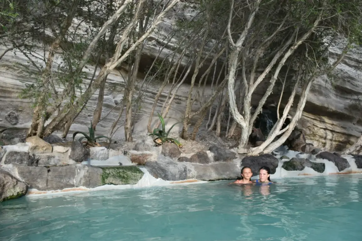Due bambine si godono le terme libere di Ischia, immerse in acque turchesi tra rocce e vegetazione rigogliosa.