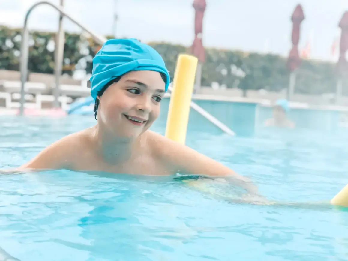 Un bambino sorridente con cuffia azzurra si diverte in piscina, un'ottima opzione per le terme Sirmione bambini.