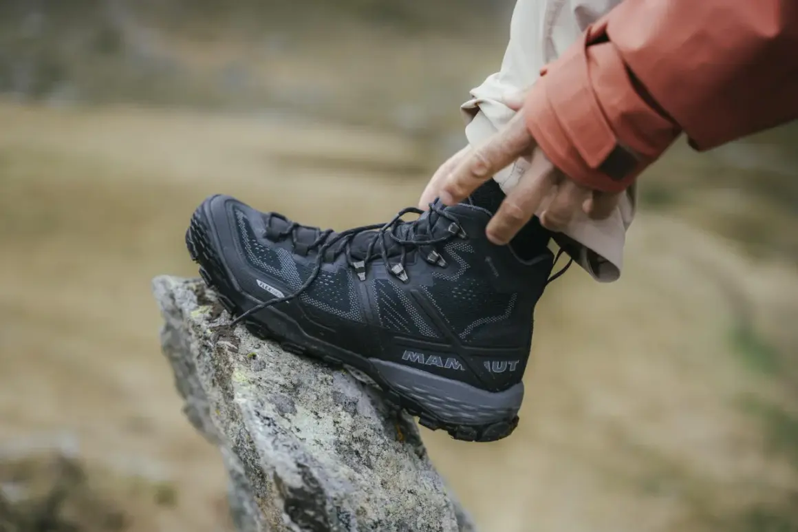 Come scegliere scarpe da trekking: un piede indossa uno scarpone nero Mammut su una roccia.