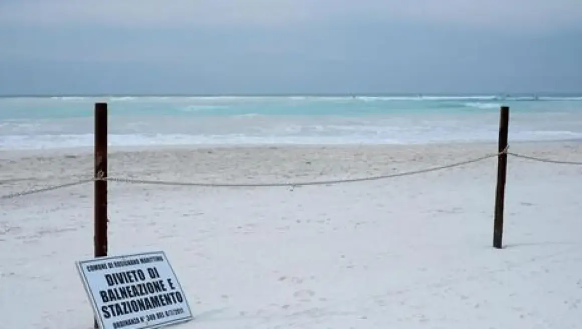Spiagge bianche deserte con mare turchese. Un cartello vieta balneazione e stazionamento.