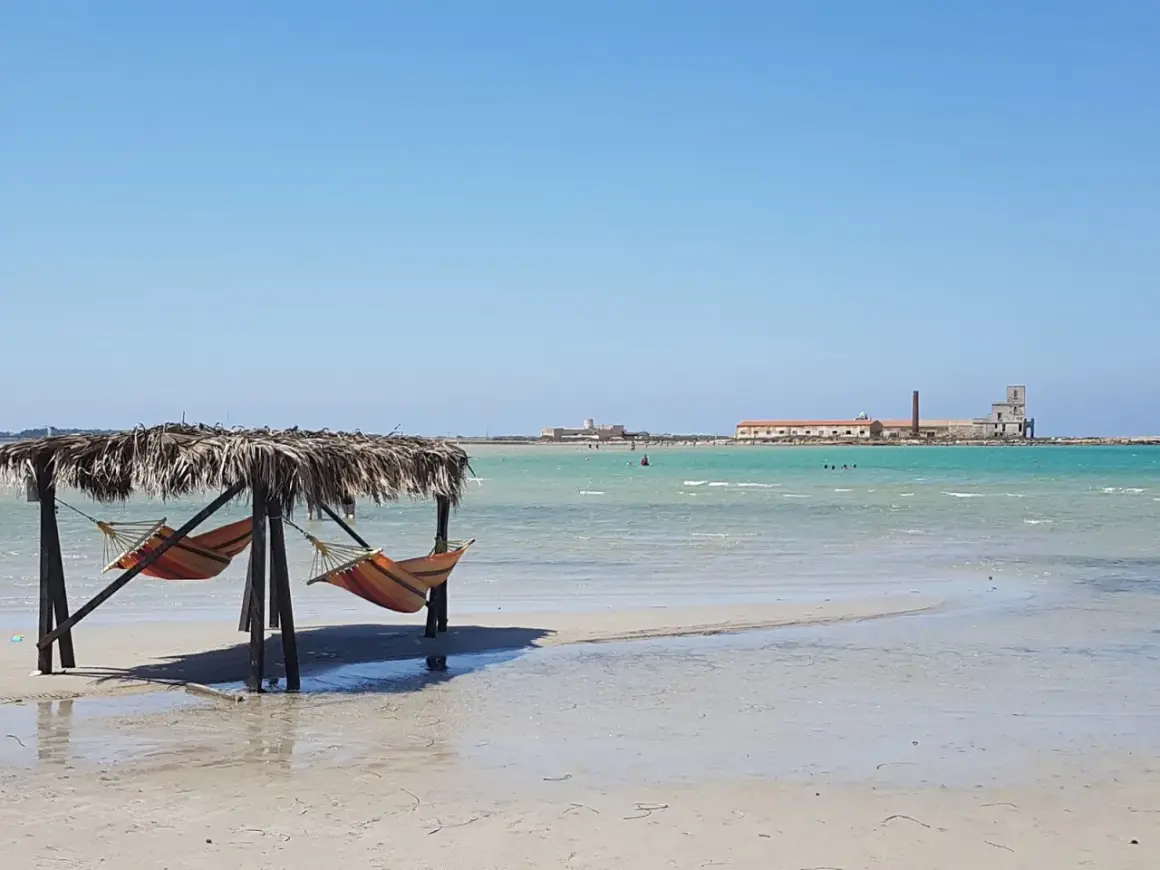 Amache colorate sotto un tetto di paglia, con il mare turchese e antichi edifici all'orizzonte. Un angolo di paradiso a San Teodoro, spiaggia rosa.