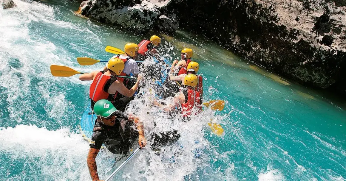 Un gruppo di persone si diverte con il rafting in Emilia Romagna, pagaiando tra spruzzi d'acqua cristallina e rocce.