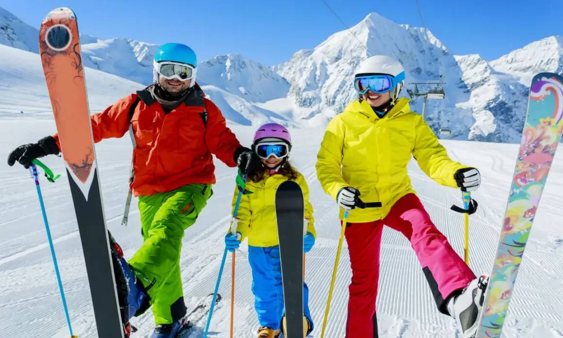 Famiglia felice sulle piste innevate, pronta dove imparare a sciare. Montagne maestose e cielo azzurro fanno da sfondo a questa avventura.