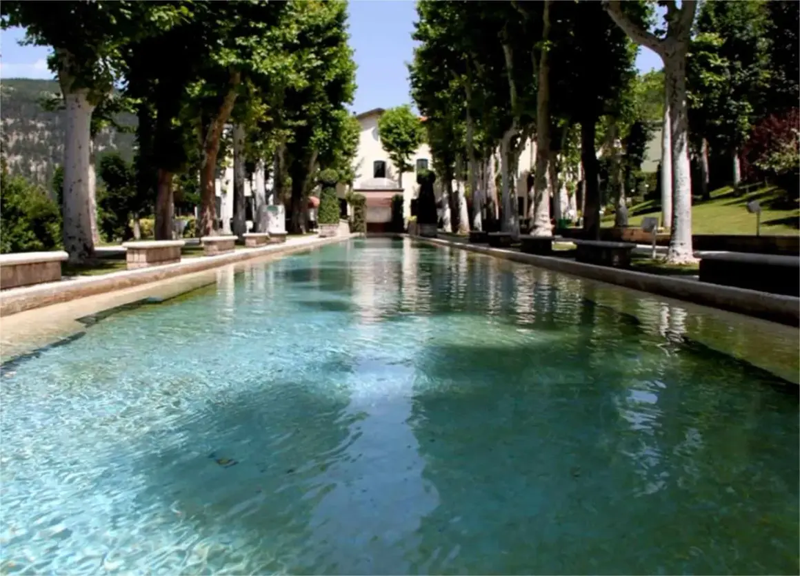 Vasca d'acqua cristallina con alberi secolari e un edificio sullo sfondo, un'oasi di pace a Caramanico Terme.