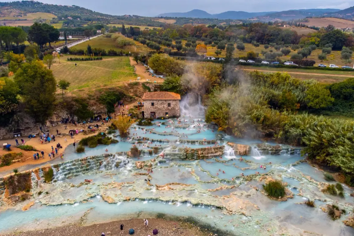 Cascate naturali con acqua azzurra e gente che si rilassa, un vero spettacolo di arte terme in un paesaggio collinare.