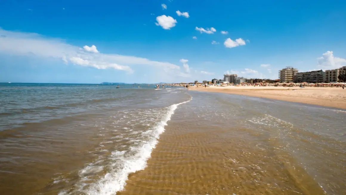Onda leggera sulla sabbia dorata, con bagnanti e hotel sullo sfondo. Un classico giorno di **mare Emilia Romagna**.
