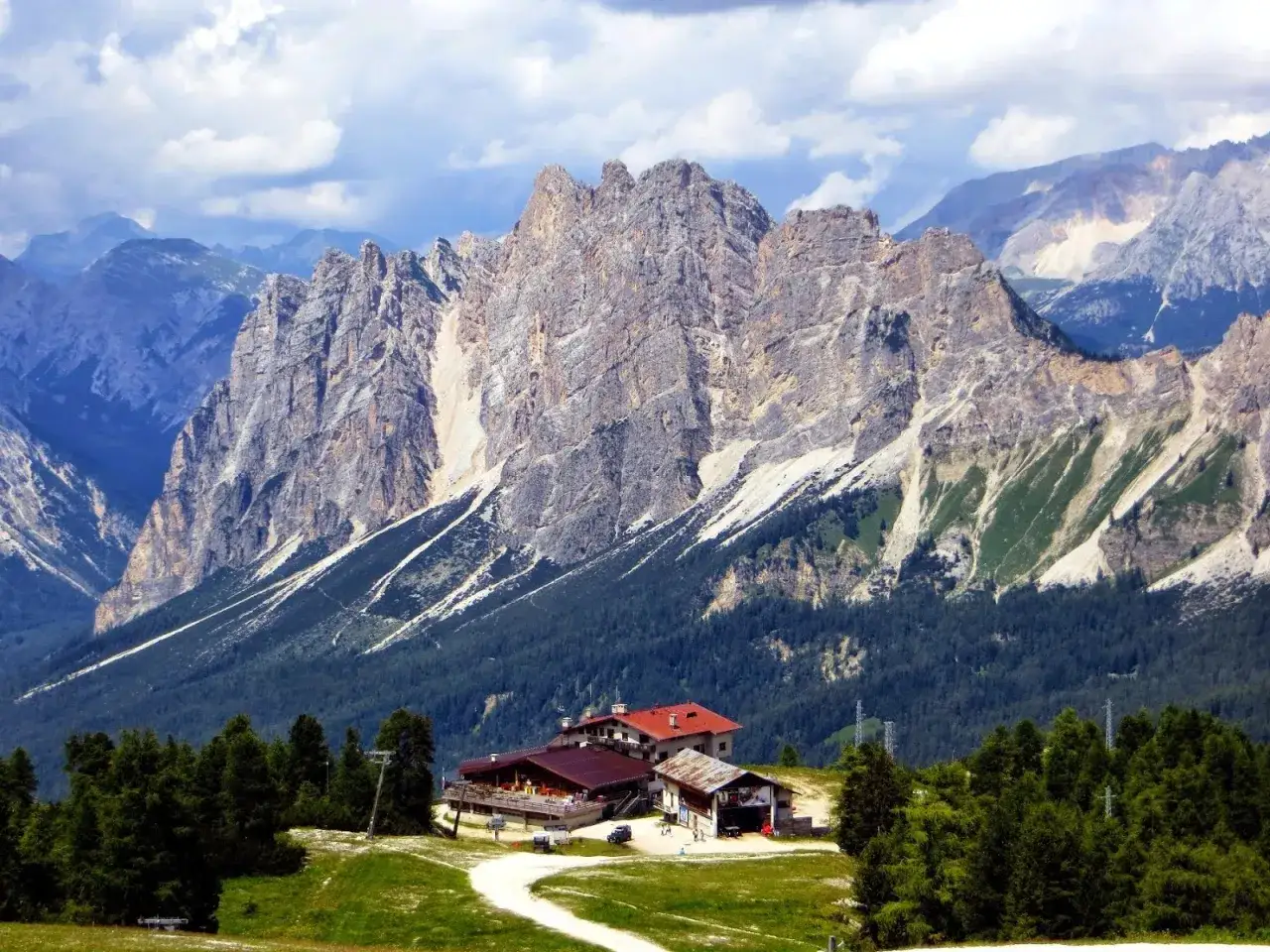 Rifugio alpino in un paesaggio mozzafiato, tra le località di montagna più belle in estate. Cime rocciose imponenti, boschi verdi e cielo azzurro.