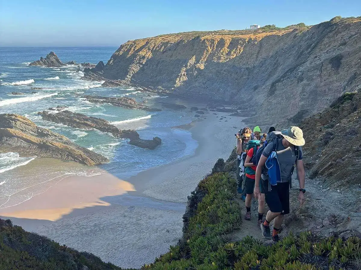 Un gruppo di escursionisti percorre il sentiero dei pescatori, con scogliere rocciose e una spiaggia dorata bagnata dall'oceano.