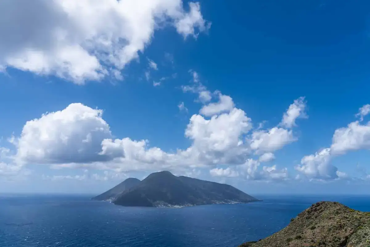 Panorami mozzafiato per la tua vacanza alle Eolie: isole vulcaniche immerse nel blu intenso del mare, sotto un cielo punteggiato di nuvole bianche.
