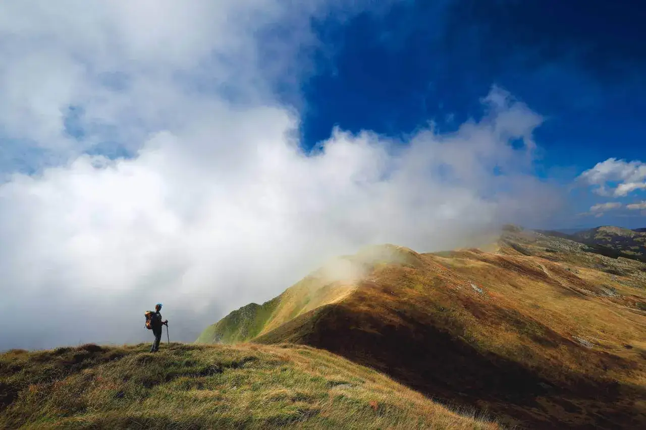 Escursionista solitario ammira i monti dell'Emilia Romagna avvolti dalla nebbia, sotto un cielo blu intenso.