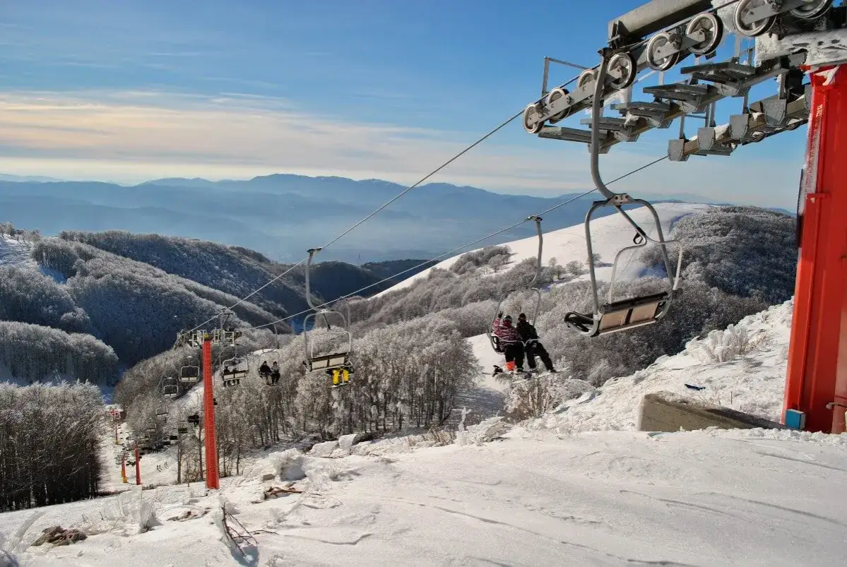 Impianti sciistici centro Italia: seggiovie trasportano sciatori su montagne innevate, con alberi coperti di brina e un cielo azzurro.