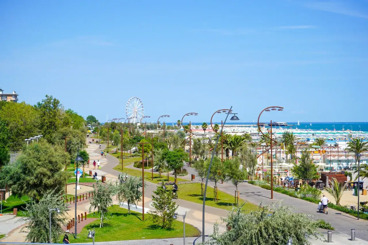 Passeggiata sul lungomare di Rimini con ruota panoramica, palme e gente che cammina e va in bicicletta.