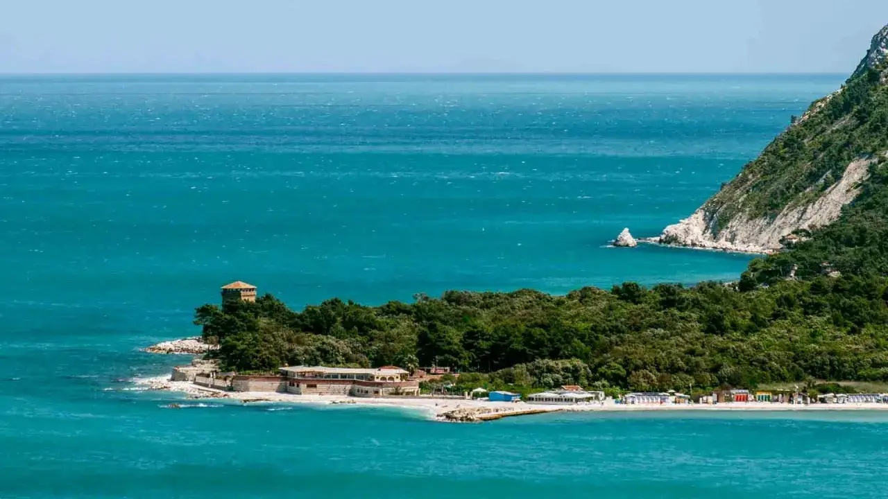 Spiagge della Riviera del Conero con mare turchese, una torre antica e una costa verdeggiante.