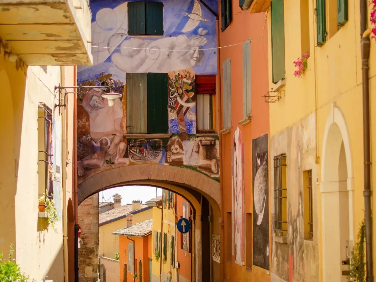Un vicolo colorato in un borgo dei murales, con opere d'arte che adornano le facciate degli edifici e un arco che conduce a un panorama di tetti.