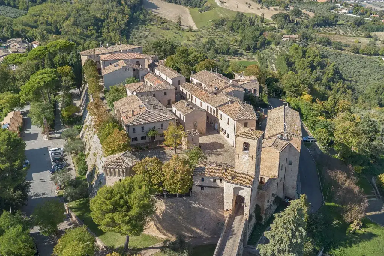 Borgo medievale di Montegridolfo cosa vedere: un incantevole panorama aereo con case in pietra, tetti in cotto e un campanile, immerso nel verde delle colline.